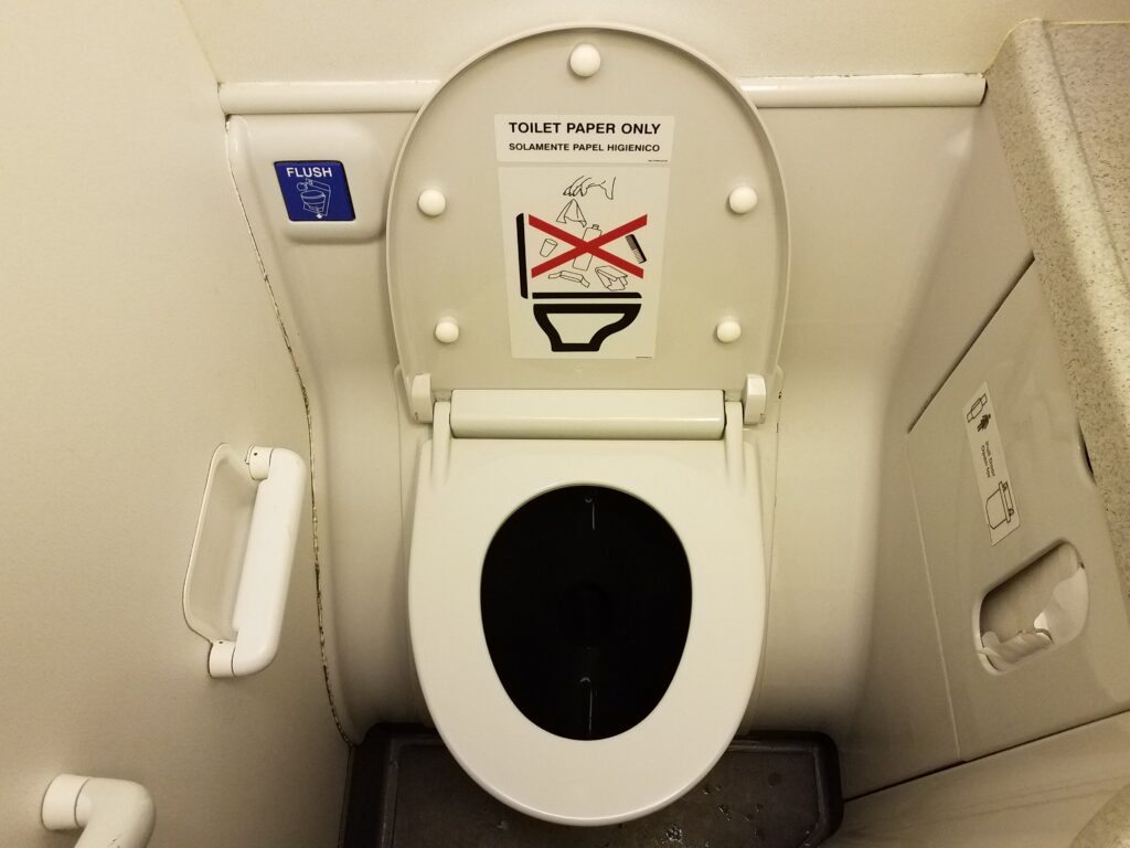 toilet paper only sign on airplane toilet lid in bathroom and blue flush button