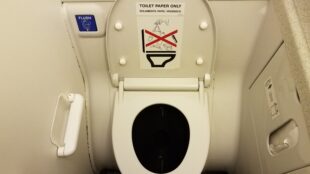 toilet paper only sign on airplane toilet lid in bathroom and blue flush button