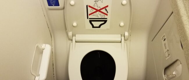 toilet paper only sign on airplane toilet lid in bathroom and blue flush button