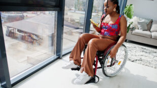 Young disabled African American woman in wheelchair at home watching at her smartphone.