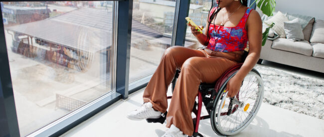 Young disabled African American woman in wheelchair at home watching at her smartphone.