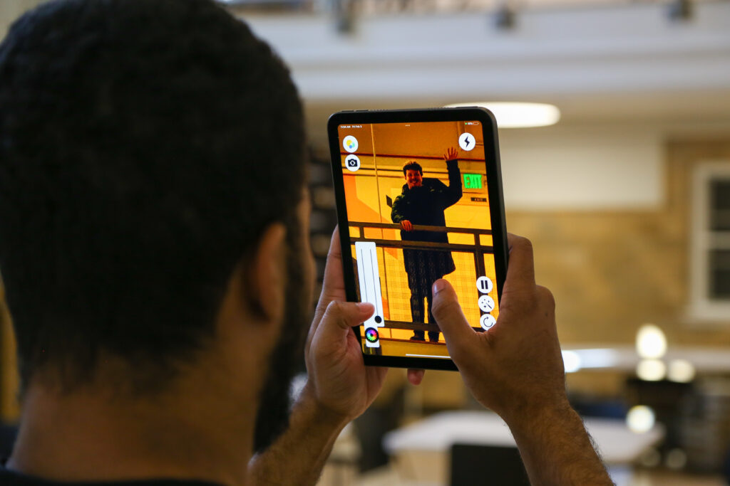 A person using the ReBokeh app on a tablet to find their friend in a public space. The friend is seen waving at the person using the app.