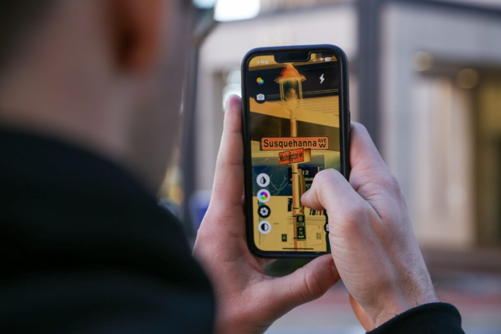 A person using the ReBokeh app to a read street sign. The person is holding a cell phone in and looking at a picture of the street sign on the screen. The street sign is for Susquehanna Avenue W and Washington Ave.