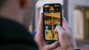 A person using the ReBokeh app to a read street sign. The person is holding a cell phone in and looking at a picture of the street sign on the screen. The street sign is for Susquehanna Avenue W and Washington Ave.