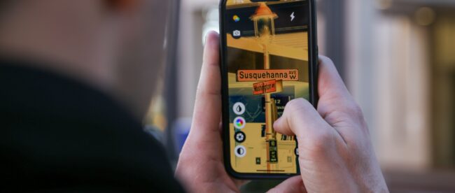 A person using the ReBokeh app to a read street sign. The person is holding a cell phone in and looking at a picture of the street sign on the screen. The street sign is for Susquehanna Avenue W and Washington Ave.