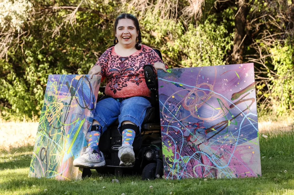 Kaya Eccles smiles as she poses for photos with two of her paintings in Logan on Wednesday, July 12, 2023