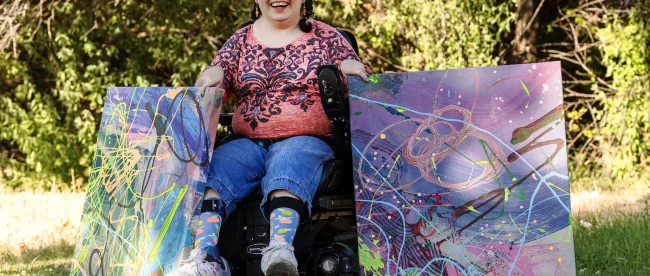 Kaya Eccles smiles as she poses for photos with two of her paintings in Logan on Wednesday, July 12, 2023