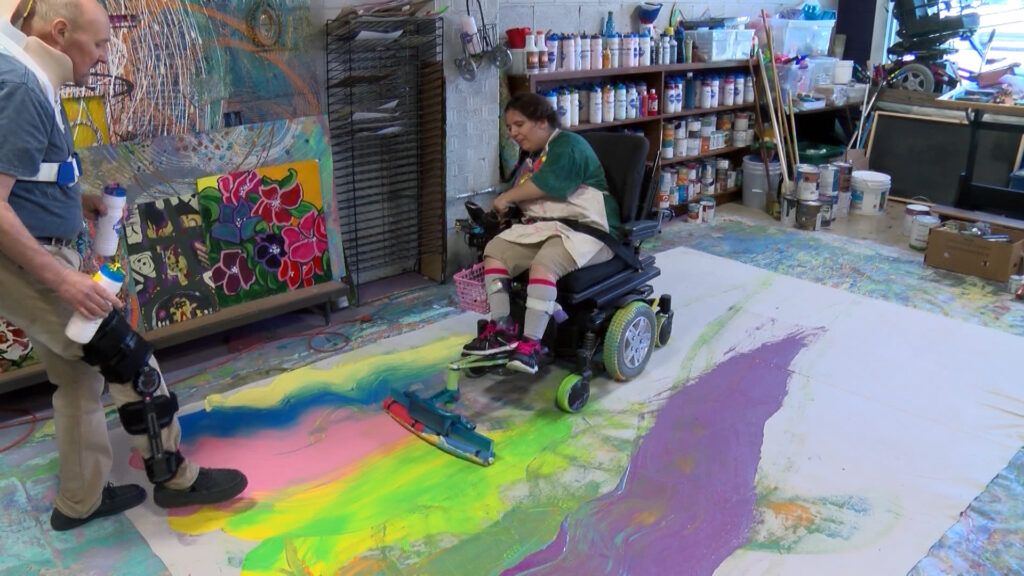 Michael Bingham helps Kaya Eccles make art with her adaptive painting tools attached to her wheelchair