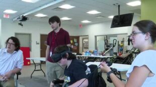 A kid in black shirt plays VR games while three others look at his game.