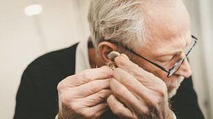 An elderly man wearing his hearing aid in his right ear.