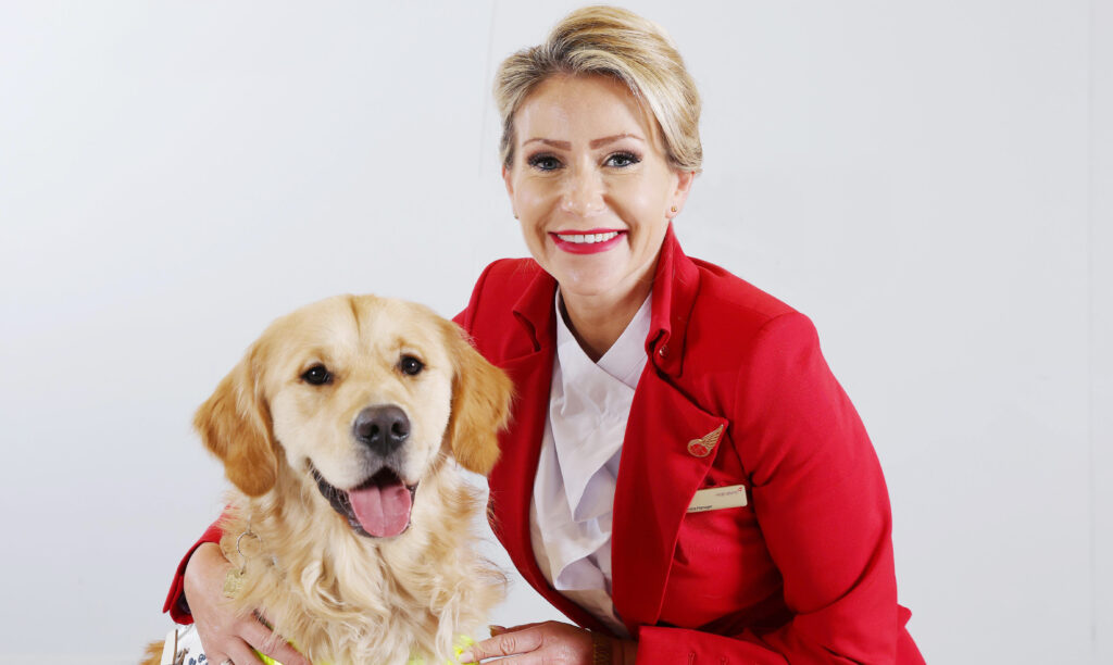 a virgin Atlantic flight crew member wearing a red jacket and white shirt is posing with a guide dog.