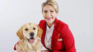 a virgin Atlantic flight crew member wearing a red jacket and white shirt is posing with a guide dog.