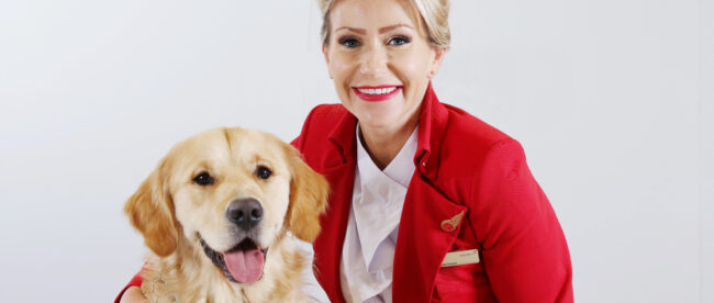 a virgin Atlantic flight crew member wearing a red jacket and white shirt is posing with a guide dog.