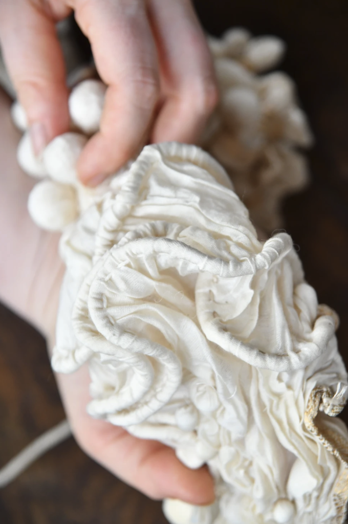 A detail shot of Sugandha's hands holding a textured silk scarf with wavy cords flowing on top of each other executed through silk fabric.