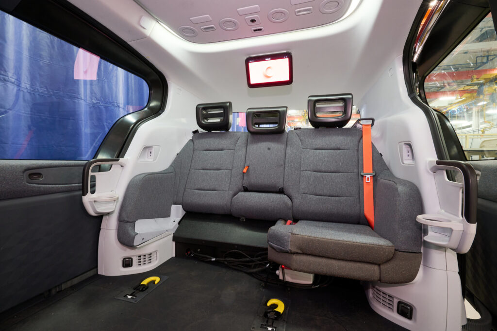 Photo shows inside of the wheelchair accessible robotaxi. There are two seats to one side and a small monitor on the ceiling.