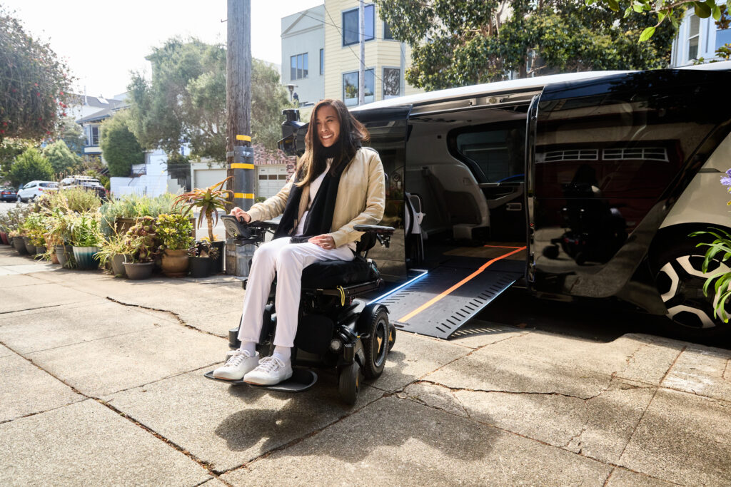 A woman in a powered wheelchair posing outside the robotaxi and smiling.