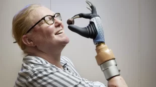 Karin seen holding a small round piece of chocolate with her prosthetic hand close to her mouth and smiling.