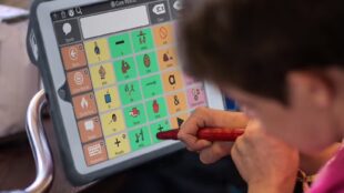 A child seen using an AAC app on a tobii device with a stylus.