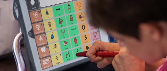 A child seen using an AAC app on a tobii device with a stylus.