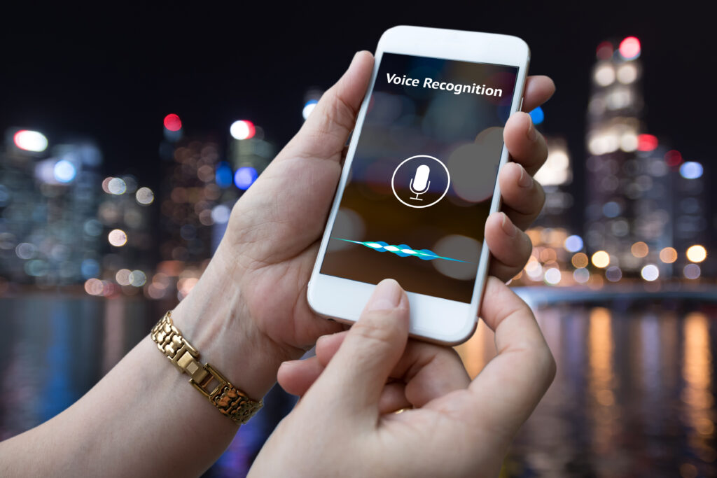 close up of a phone with the text "voice recognition" and microphone icon. It is held upclose in both hands by someone.