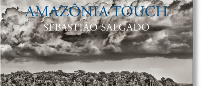 A black and white photo of a small island in the middle of a large body of water surrounded by clouds. The text Amazon Touch Sebastian Salgado is laid on top of the image.