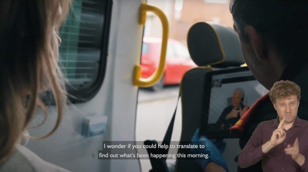 The image depicts an emergency situation where a paramedic uses an iPad to facilitate communication with a Deaf patient. The iPad is running the SignVideo app, which connects to a sign language interpreter displayed on the screen. The interpreter is helping the paramedic understand and communicate with the patient, who is providing information about their condition. This setup helps bridge the communication gap, ensuring that the patient can convey their needs effectively and receive appropriate medical care. The inclusion of subtitles and a visible interpreter in the bottom right corner emphasizes the accessibility of the service for the Deaf community.