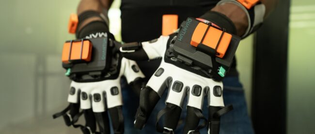 2025_elly_dsc00350 Close-up of motion capture gloves with black and white design featuring orange sensor pads on the back of the hands and fingertips, used for recording sign language movements