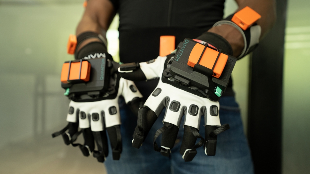 Close-up of motion capture gloves with black and white design featuring orange sensor pads on the back of the hands and fingertips, used for recording sign language movements