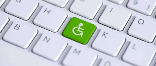 Green key with wheelchair icon on white laptop keyboard. Accessibility disability computer symbol