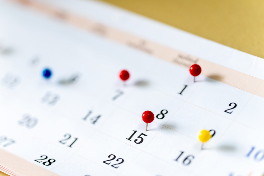 Close-up of a paper calendar with red and yellow pins marking important dates, representing the downloadable 2026 Disability Awareness & Assistive Technology calendar.