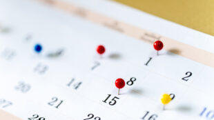 Close-up of a paper calendar with red and yellow pins marking important dates, representing the downloadable 2026 Disability Awareness & Assistive Technology calendar.
