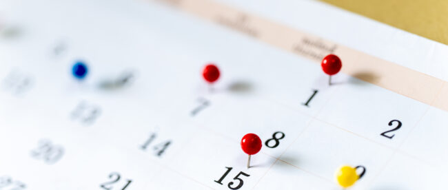 Close-up of a paper calendar with red and yellow pins marking important dates, representing the downloadable 2026 Disability Awareness & Assistive Technology calendar.