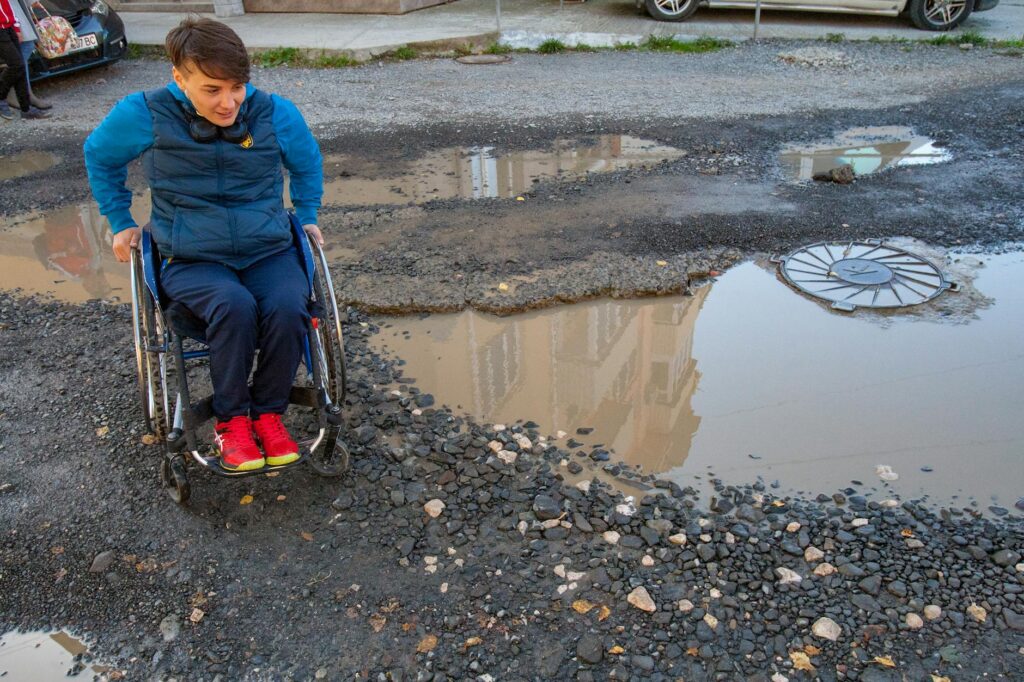 PErson in a wheelchair trying to manoeuvre a big puddle of water on the street.