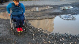 PErson in a wheelchair trying to manoeuvre a big puddle of water on the street.