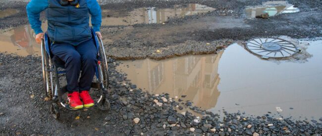 PErson in a wheelchair trying to manoeuvre a big puddle of water on the street.