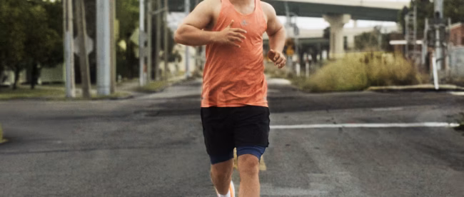 A man with Down syndrome, athlete Chris Nikic, running confidently down a paved road in a bright orange tank top and the orange adidas Supernova Rise 3 Adaptive running shoes.